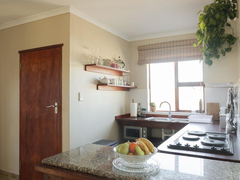 A functional kitchen featuring granite countertops, a built-in hob, stainless steel sink, and wooden shelving, offering a practical layout with natural light.