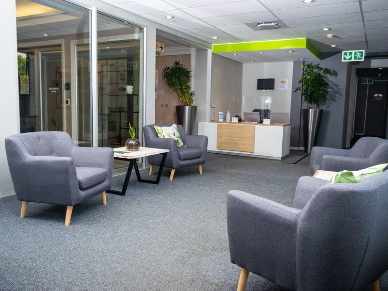 A professional office reception area featuring a modern reception desk, glass-partitioned offices, carpeted flooring, and recessed ceiling lighting.