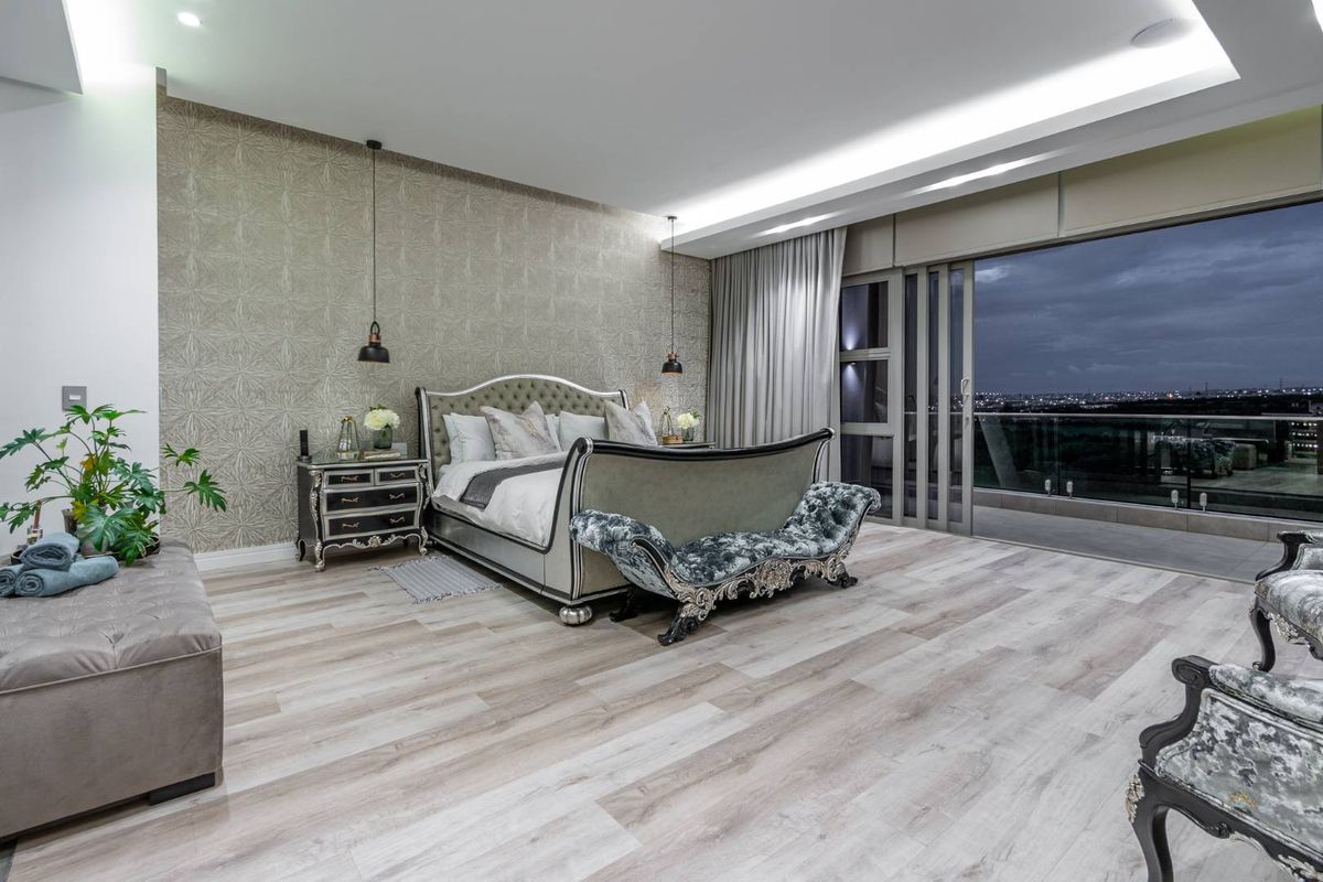 Spacious master bedroom featuring modern wood-look flooring, textured feature wallpaper, recessed ceiling lighting, and large sliding glass doors opening to a private balcony.