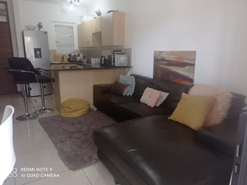 Open plan living area featuring a kitchen with granite countertops and breakfast bar, seamlessly flowing into the lounge space with tiled flooring throughout.