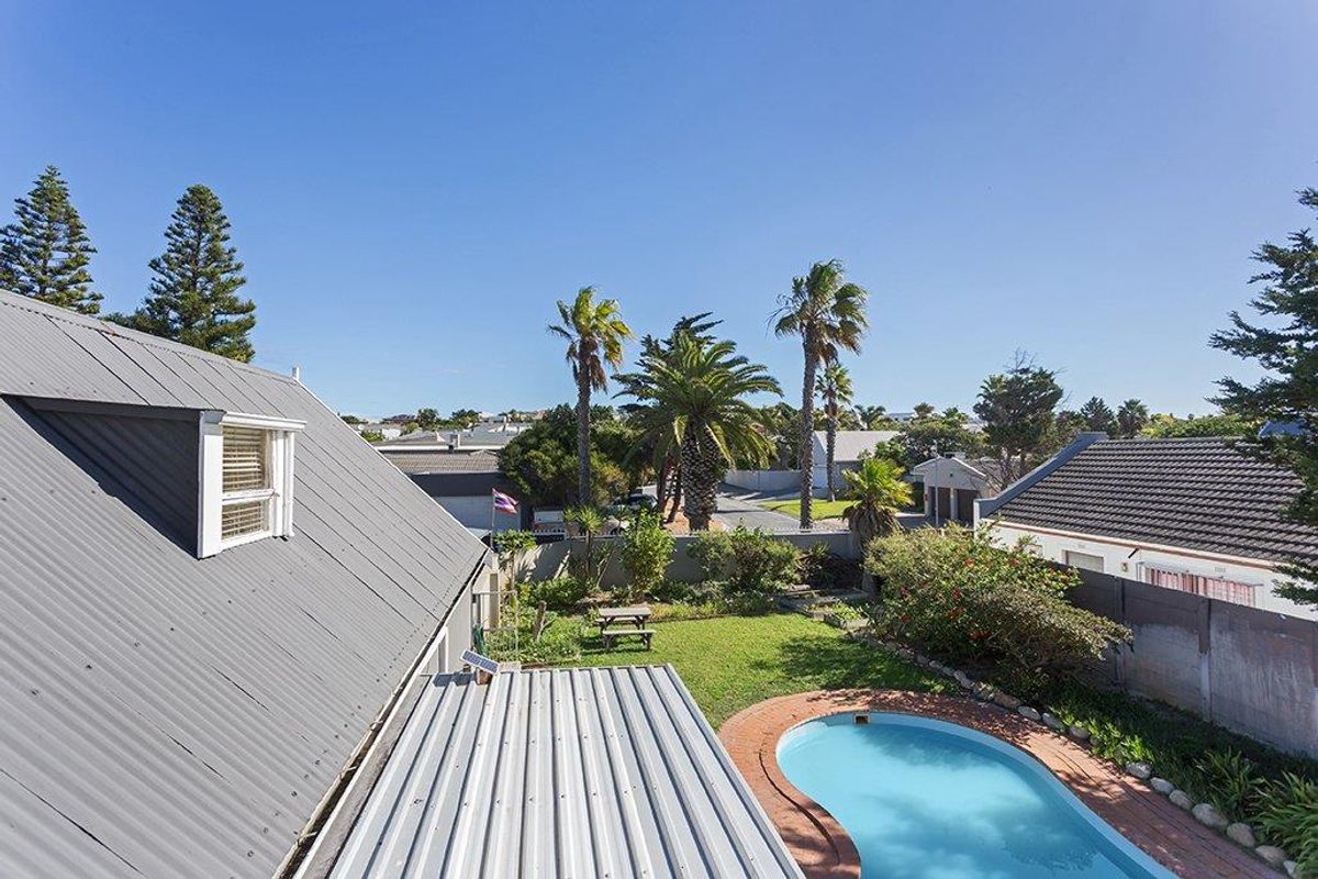 Aerial view of the property backyard featuring a swimming pool, landscaped garden, and corrugated metal roofing on the main structure.