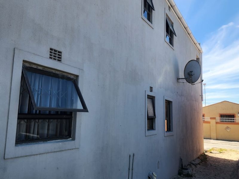 Side elevation of the property featuring plastered walls, top-hung windows with security bars, and external plumbing fixtures.