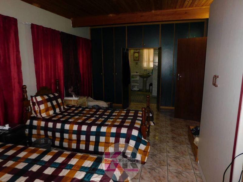 A bedroom featuring built-in cupboards, tiled flooring, and a timber ceiling, with an adjoining bathroom visible through the doorway.