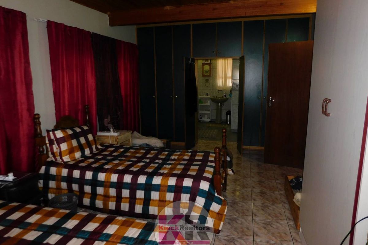A bedroom featuring built-in cupboards, tiled flooring, and a timber ceiling, with an adjoining bathroom visible through the doorway.