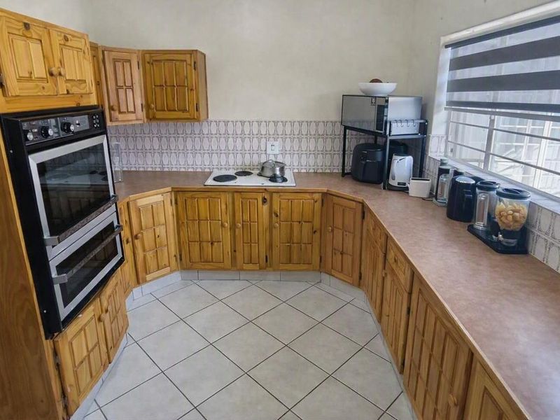 A functional kitchen featuring traditional wooden cabinetry, laminate countertops, an eye-level oven, and an electric hob with tiled splashback.