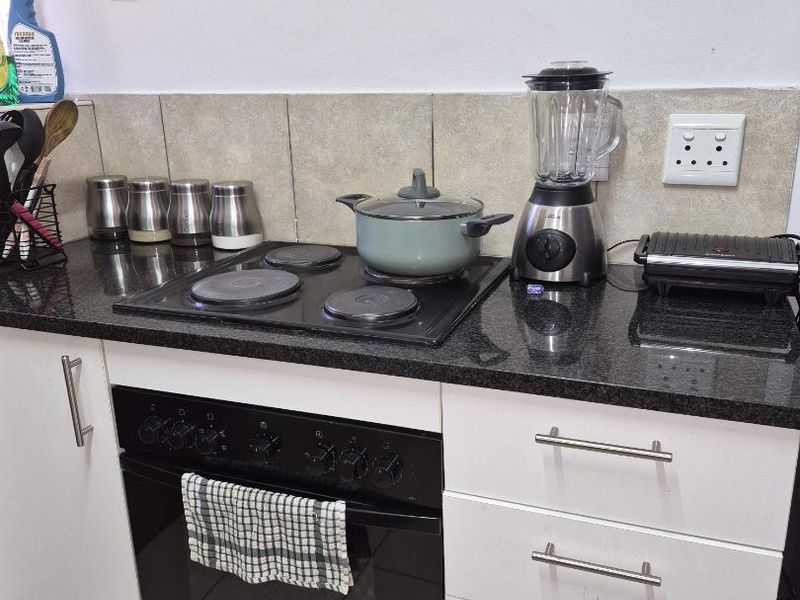 A functional kitchen area featuring a granite countertop, built-in electric hob, oven, and white cabinetry with a tiled backsplash.