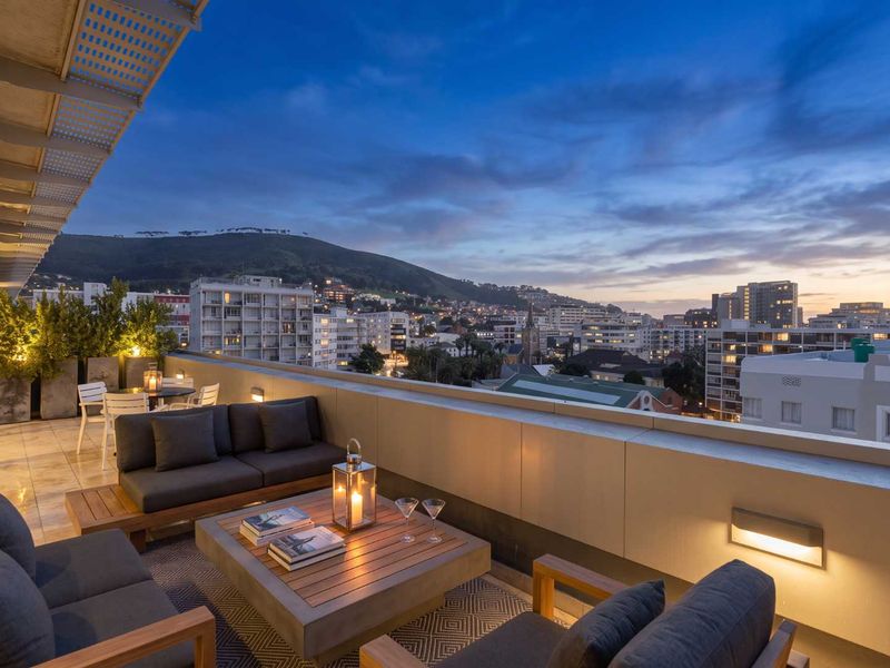 Spacious penthouse balcony featuring tiled flooring, integrated wall lighting, and panoramic city and mountain views at dusk.