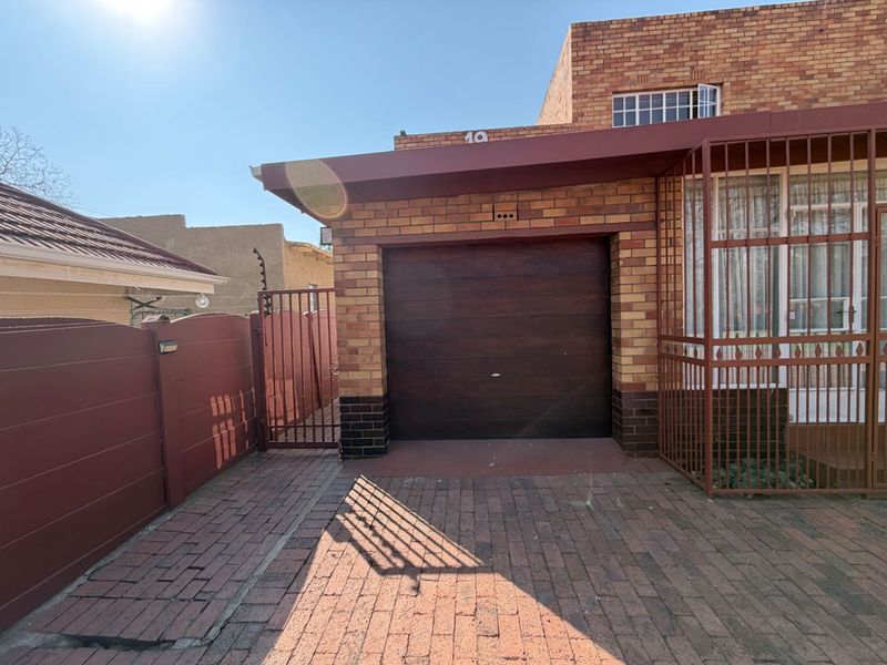 Front exterior view of the property featuring a brick facade, a single garage door, and a paved driveway with secure perimeter fencing.