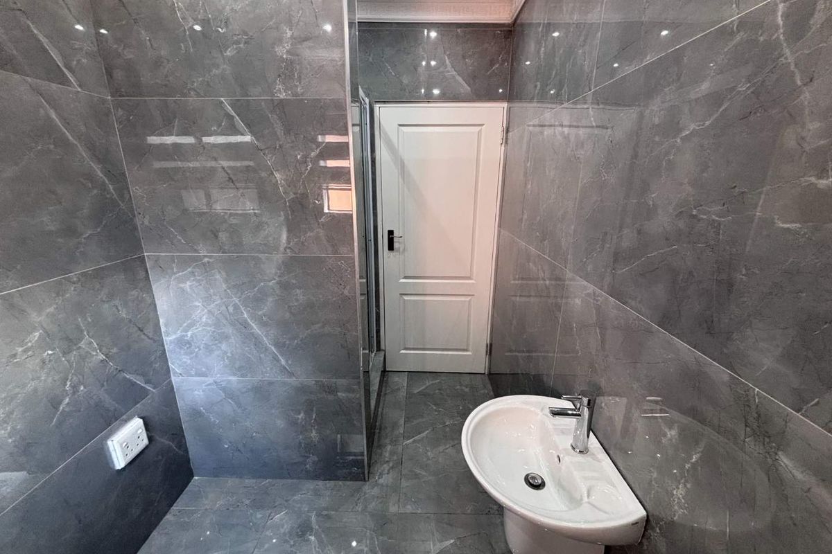 Modern bathroom featuring floor-to-ceiling grey marble-look tiles, a pedestal basin with chrome mixer tap, and a white panel door.