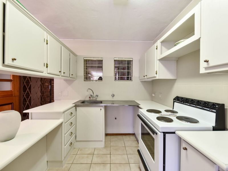 A functional kitchen featuring white built-in cabinetry, a stainless steel sink, tiled splashbacks, and a freestanding electric stove.