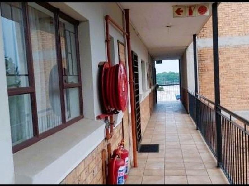 An exterior apartment corridor featuring tiled flooring, metal safety railings, and installed fire safety equipment including a hose reel and extinguishers.