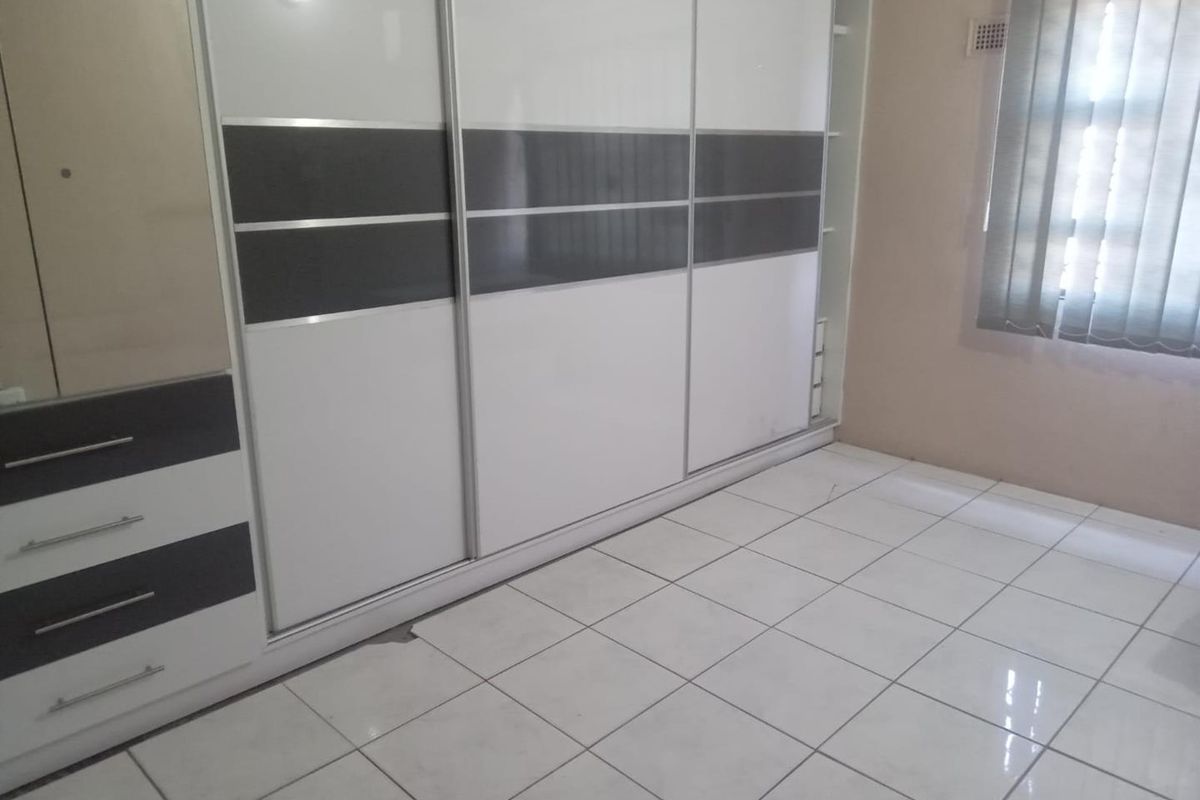 A clean, empty bedroom featuring modern built-in sliding door wardrobes, neutral ceramic floor tiles, and vertical window blinds.
