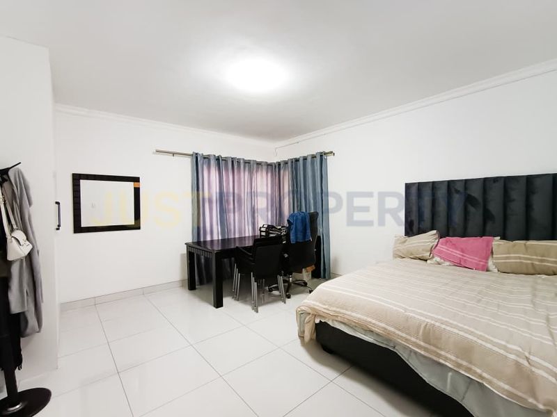 Spacious bedroom featuring neutral tiled flooring, built-in storage, and large windows with curtain rails, offering a clean and functional living space.