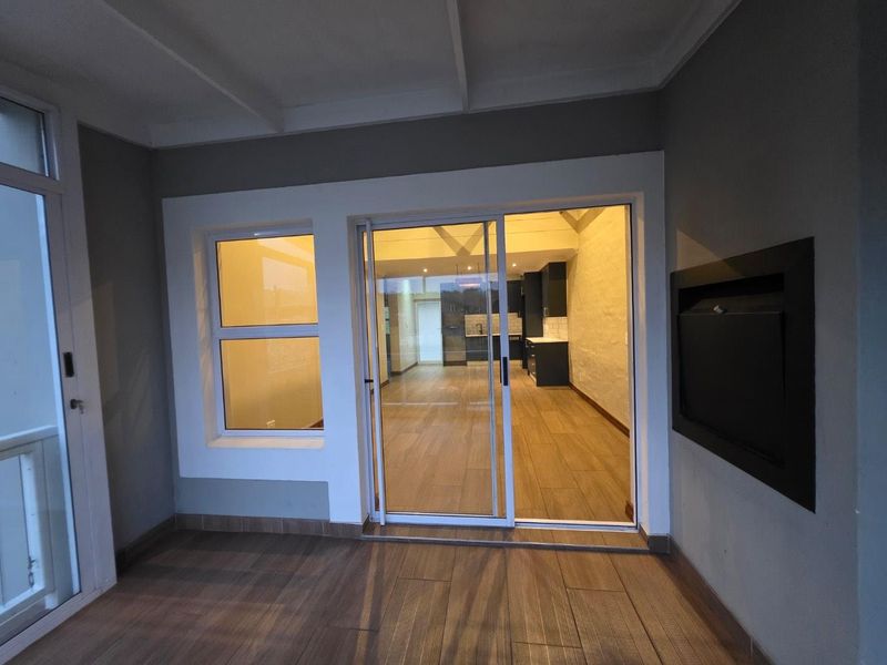A covered patio area featuring tiled flooring, a built-in fireplace, and sliding glass doors providing access to the interior living space.