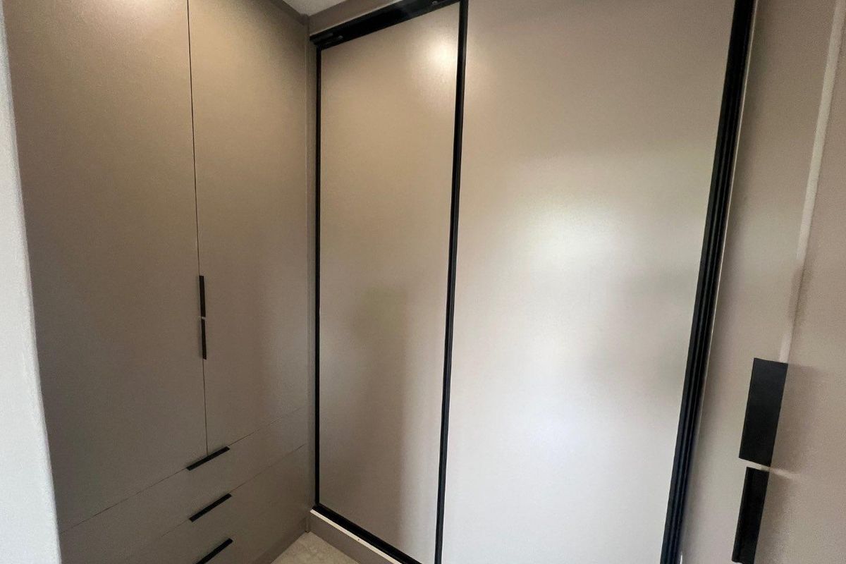 A modern bedroom featuring built-in floor-to-ceiling cabinetry with sleek matte finishes and integrated sliding doors for ample storage space.