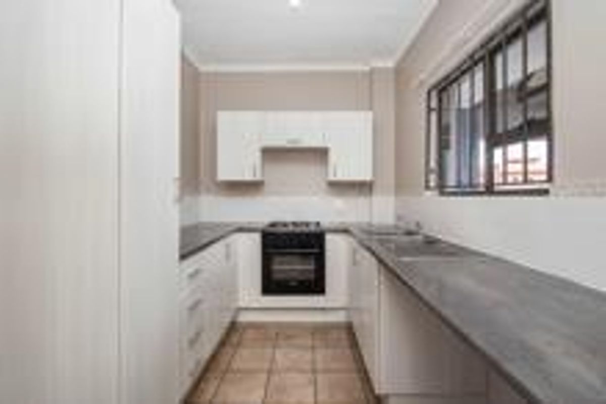A clean, functional kitchen featuring white cabinetry, dark countertops, a built-in oven and hob, and tiled flooring.