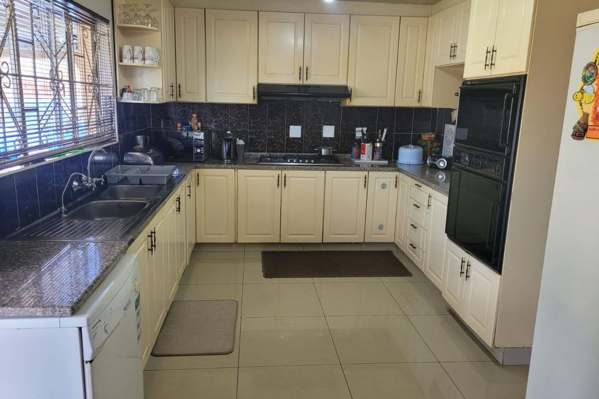 A functional kitchen featuring cream-colored cabinetry, granite countertops, a gas hob, extractor fan, and built-in oven with tiled flooring and backsplash.