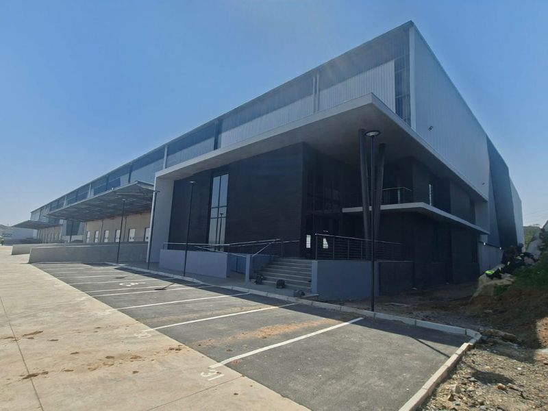 Modern industrial warehouse facility featuring a large concrete loading area, asphalt parking, and contemporary metal cladding facade.