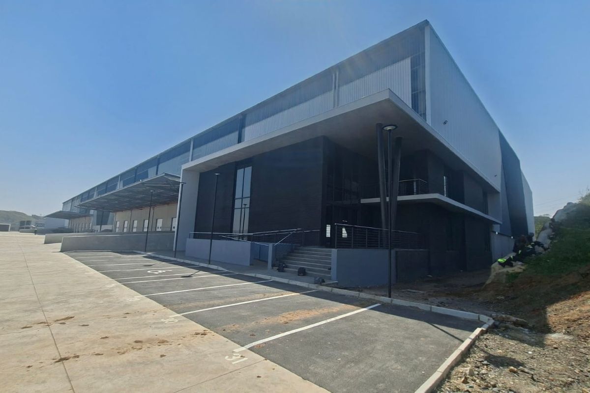 Modern industrial warehouse facility featuring a large concrete loading area, asphalt parking, and contemporary metal cladding facade.