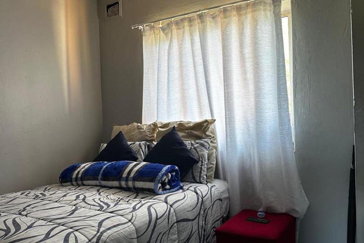A compact bedroom featuring tiled flooring, a window with curtain treatments, and a ceiling vent.