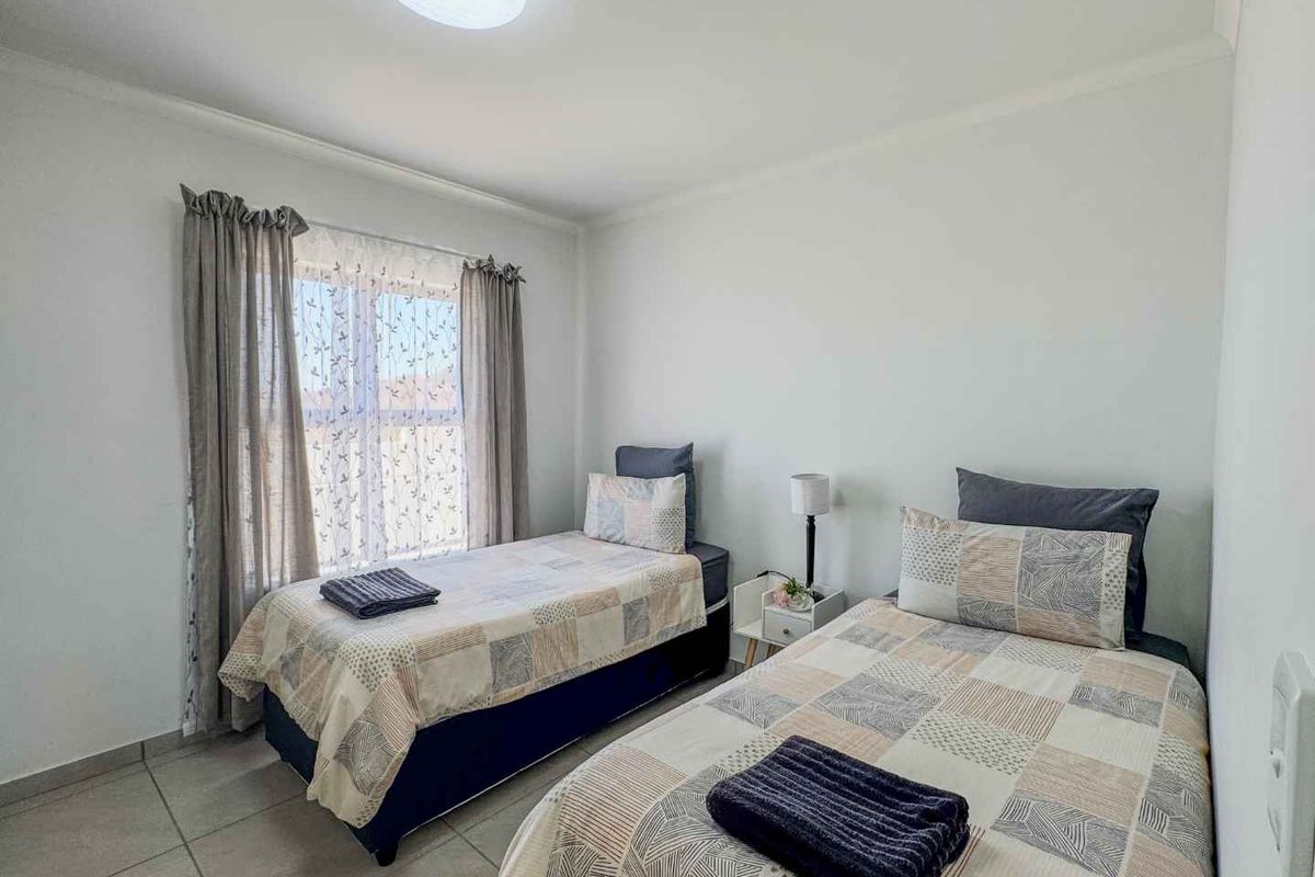 A functional bedroom featuring tiled flooring, neutral walls, and a window with curtain treatments.