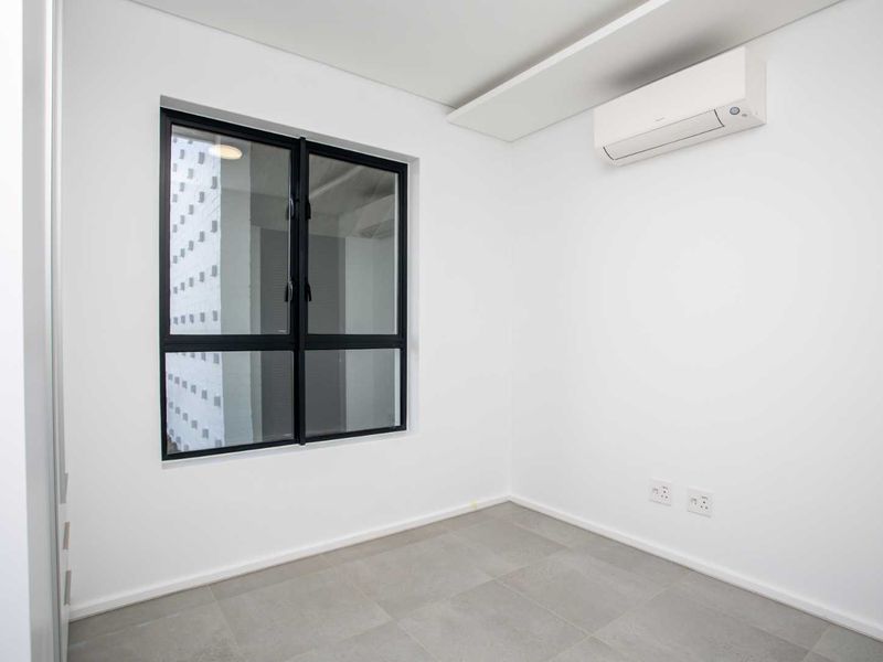 A clean, modern, and empty bedroom featuring neutral tiled flooring, a black-framed window, and a wall-mounted air conditioning unit.