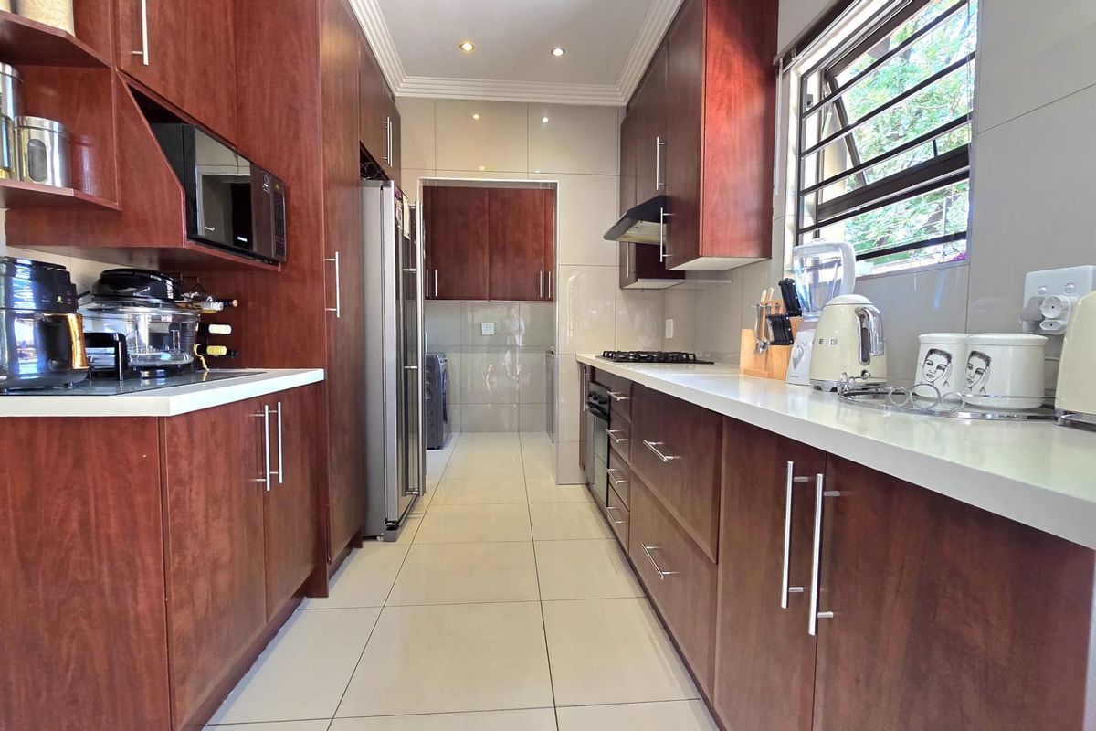 A well-maintained galley-style kitchen featuring rich wood cabinetry, stone countertops, built-in oven, gas hob, and an integrated extractor fan.
