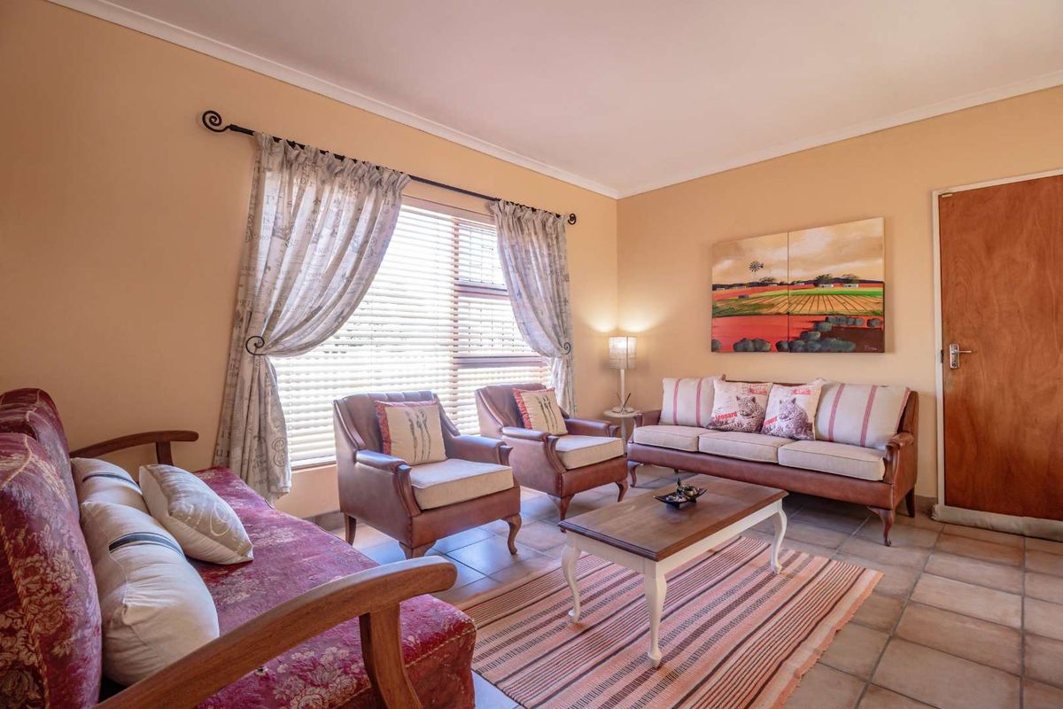 A comfortable living room featuring tiled flooring, a large window with blinds, and a solid wood door.