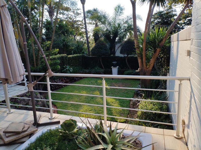 A raised patio area featuring a metal balustrade and a built-in planter, overlooking a lush, well-maintained private garden.