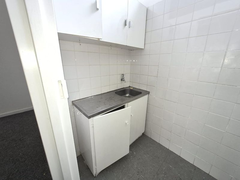 A compact utility or scullery area featuring a stainless steel sink, wall-mounted tap, and built-in white cabinetry with tiled wall finishes.