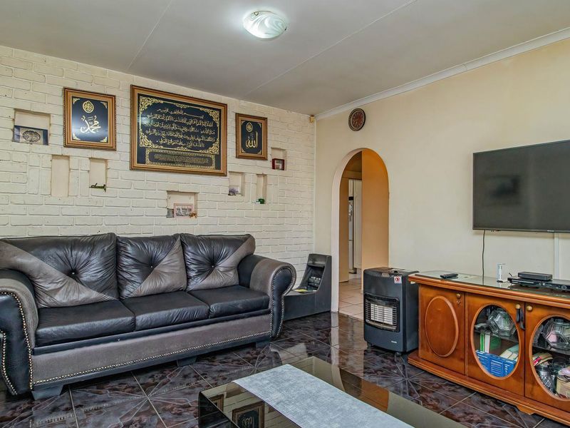 A living room featuring an exposed brick feature wall, tiled flooring, and an arched doorway leading to adjacent living spaces.