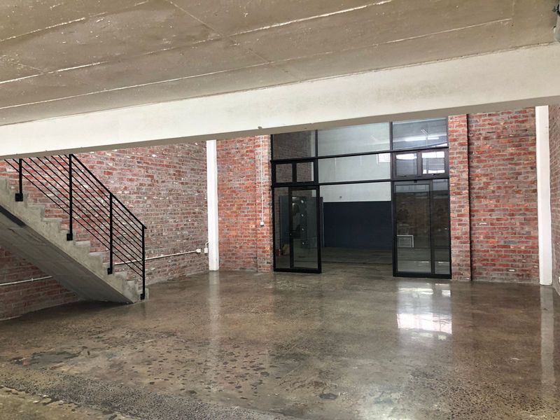 Spacious open-plan industrial style area featuring exposed brick walls, polished concrete floors, and a concrete staircase with a modern metal balustrade.