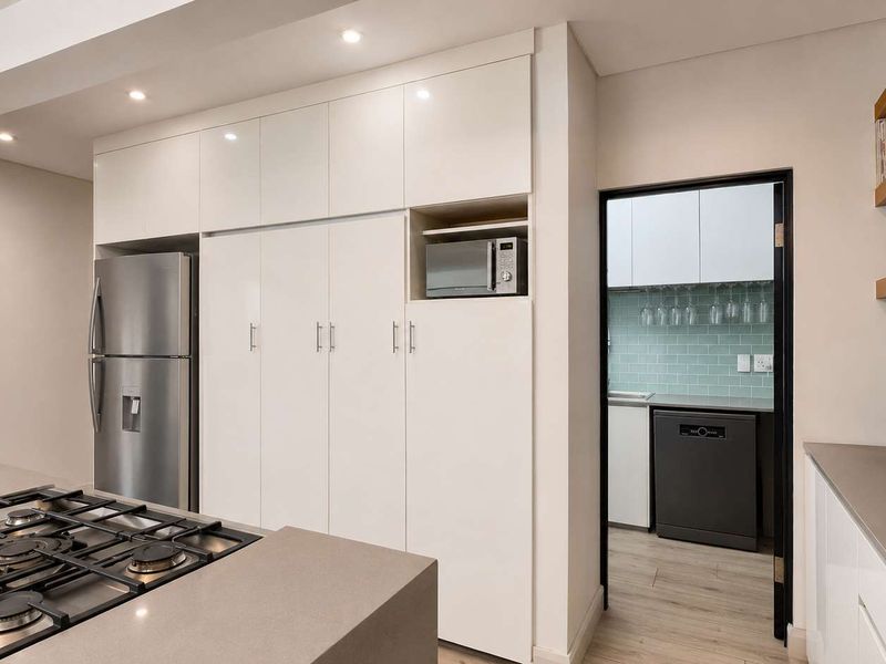Modern kitchen featuring stone countertops, a gas hob, sleek white cabinetry, and a convenient adjoining scullery area with additional storage and workspace.