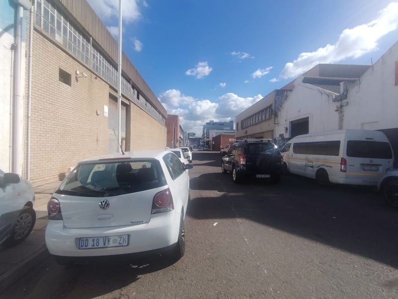 Street view of an industrial area featuring brick warehouse buildings with roller shutter doors and on-street parking.