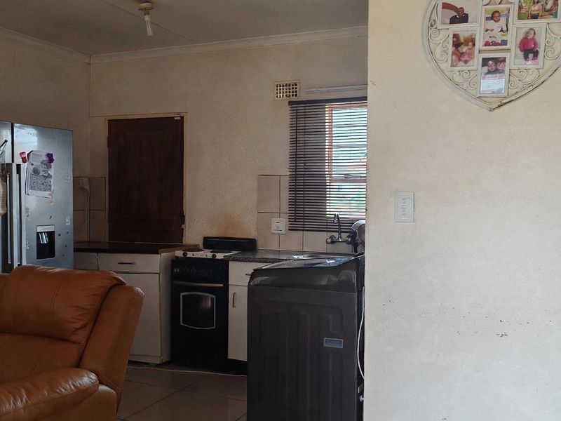 A compact kitchen area featuring built-in cabinetry, a freestanding stove, and tiled flooring, offering a functional layout in need of cosmetic updates.