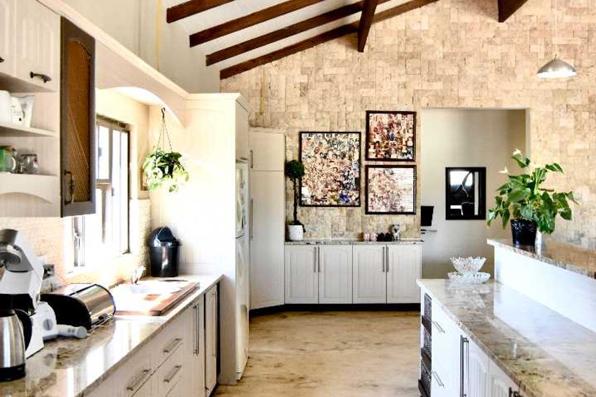 Spacious kitchen featuring exposed timber beams, stone cladding, granite countertops, and a gas hob, set against a rustic concrete floor.