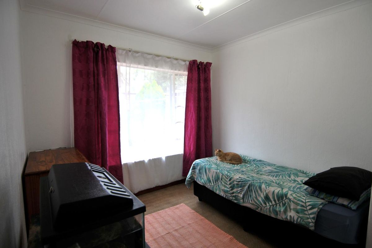 A functional bedroom featuring neutral walls, a large window with curtains, and carpeted flooring.