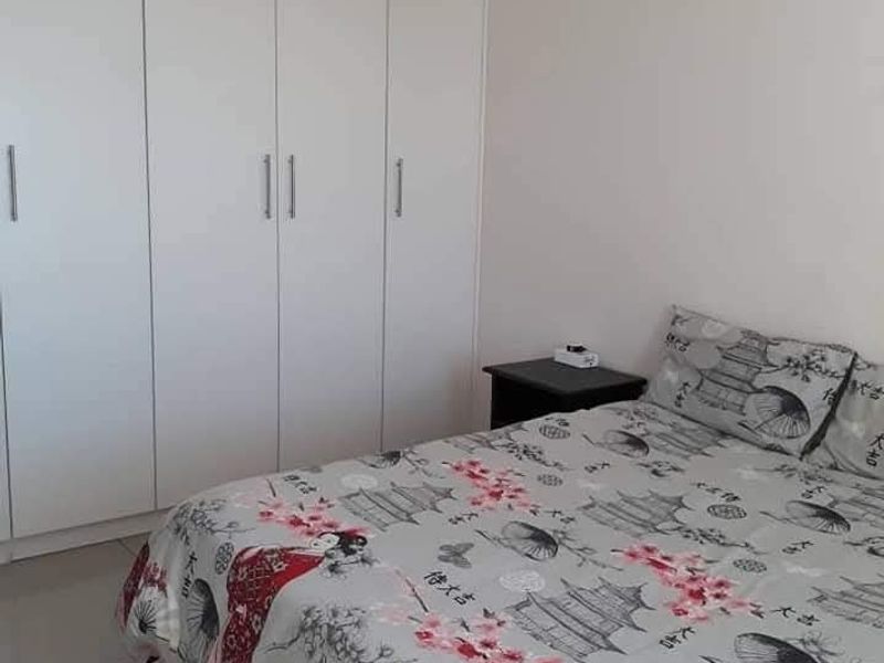 A clean bedroom featuring neutral tiled flooring and ample storage space provided by floor-to-ceiling built-in cupboards.