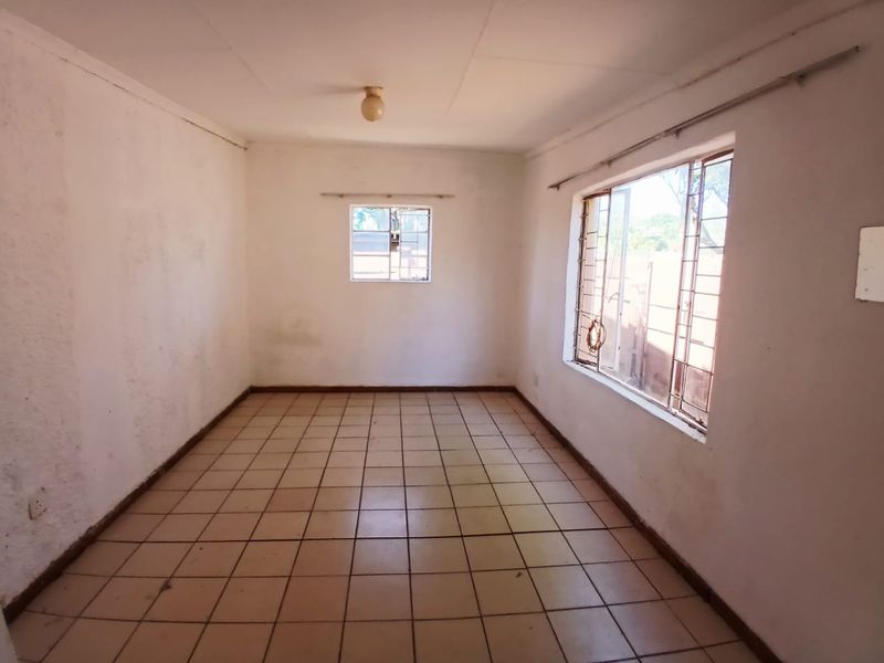An empty, sunlit living area featuring tiled flooring and security bars on the windows, offering a blank canvas for renovation.