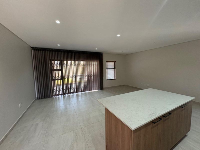 Spacious open-plan living area featuring modern porcelain floor tiles, recessed lighting, and a central kitchen island with a stone countertop.