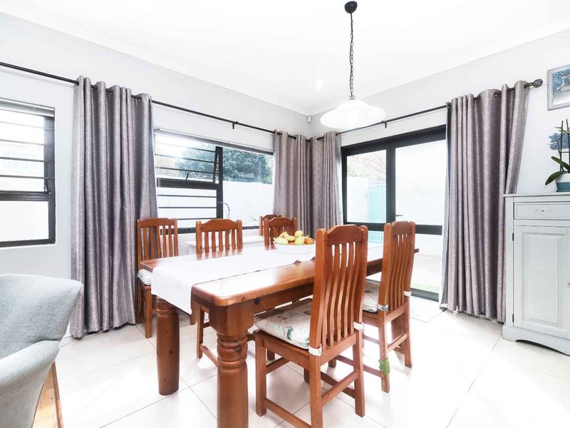 Bright dining room featuring neutral tiled flooring, large aluminium windows, and a sliding glass door providing access to the outdoor area.