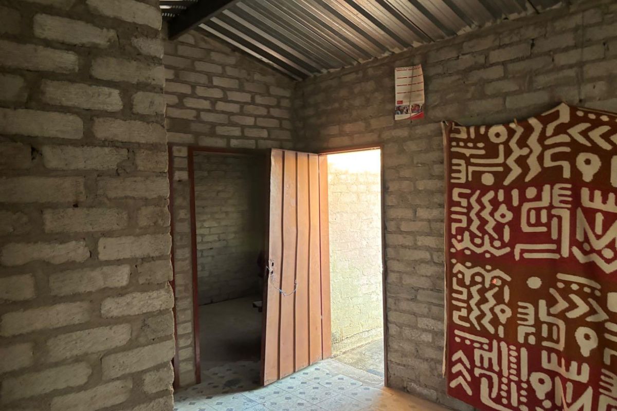 A basic interior space featuring exposed brick walls, tiled flooring, and a corrugated metal roof, providing a rustic and functional layout.