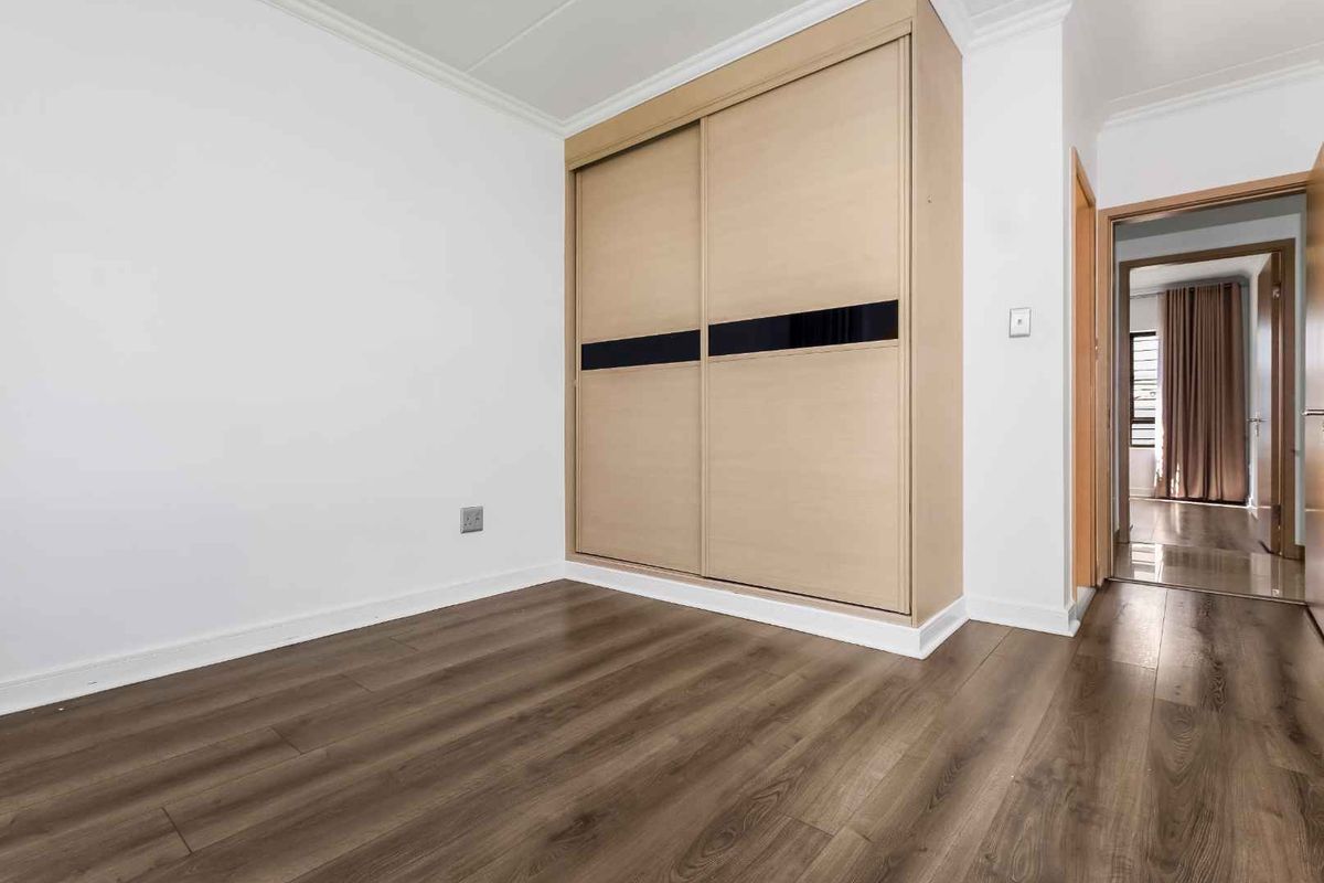 A bright, empty bedroom featuring modern laminate flooring and a large built-in sliding door wardrobe with a contemporary finish.