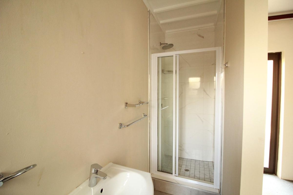 A functional bathroom featuring a shower enclosure with tiled walls and a wall-mounted basin with chrome fixtures.