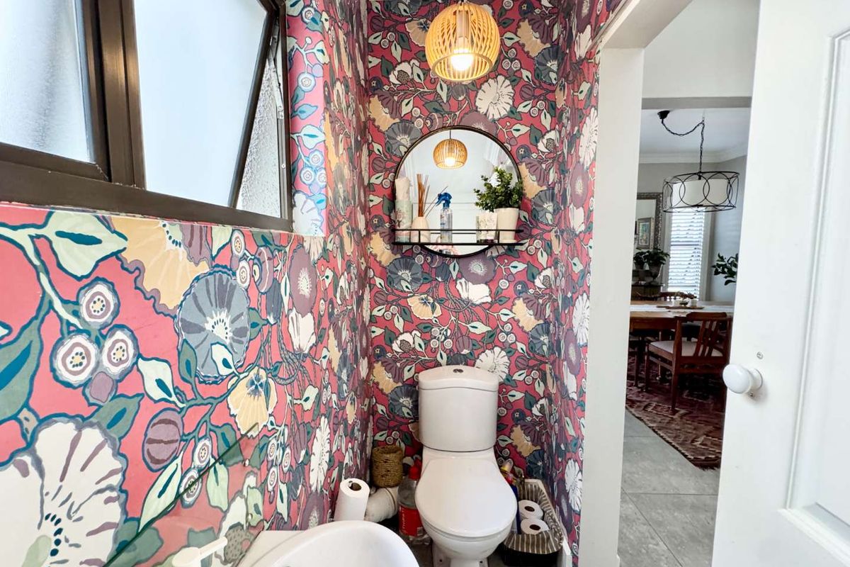 A compact powder room featuring bold floral wallpaper, a wall-mounted basin, and a standard toilet, with direct access to the adjacent dining area.