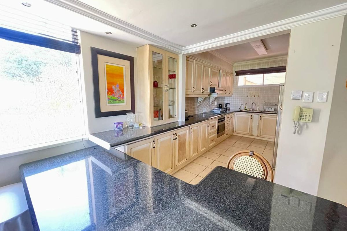 A functional kitchen featuring dark granite countertops, light-toned cabinetry, tiled flooring, and a breakfast bar area with integrated cooking appliances.