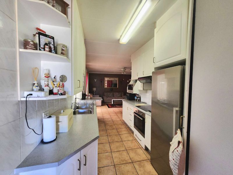 A functional galley-style kitchen featuring built-in cabinetry, laminate countertops, and integrated appliances, leading into an open-plan living area with tiled flooring throughout.