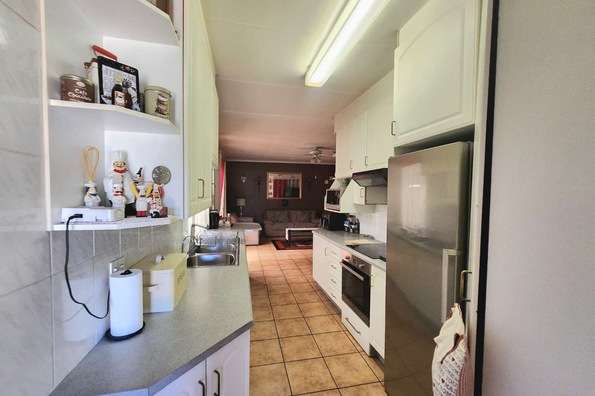 A functional galley-style kitchen featuring built-in cabinetry, laminate countertops, and integrated appliances, leading into an open-plan living area with tiled flooring throughout.