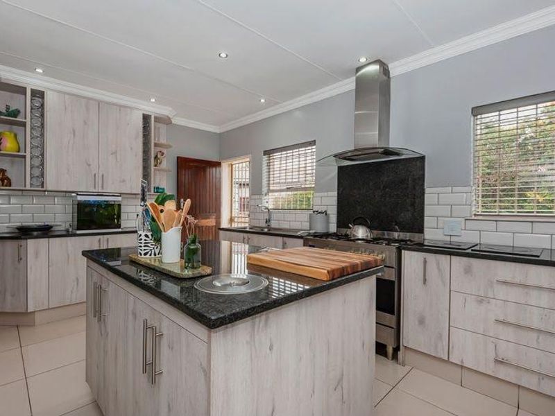 Modern kitchen featuring a central island with granite countertops, stainless steel gas stove, extractor fan, subway tile backsplash, and ample built-in cabinetry.