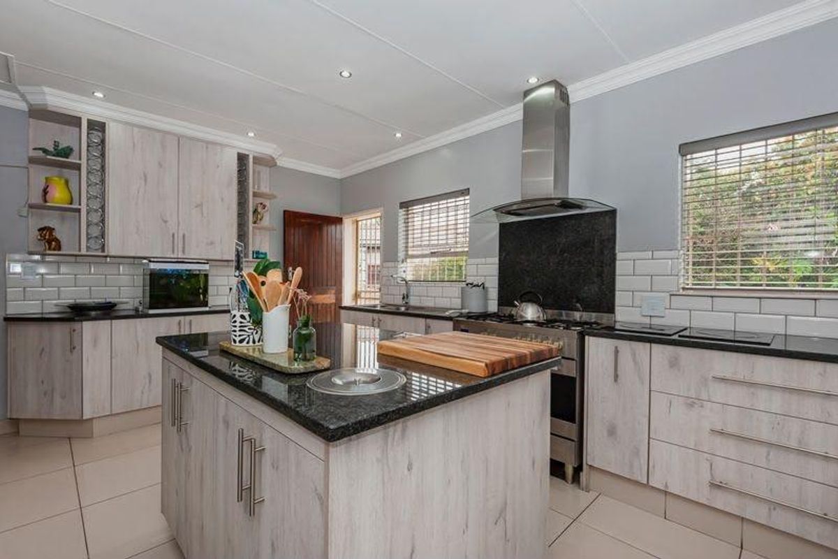 Modern kitchen featuring a central island with granite countertops, stainless steel gas stove, extractor fan, subway tile backsplash, and ample built-in cabinetry.